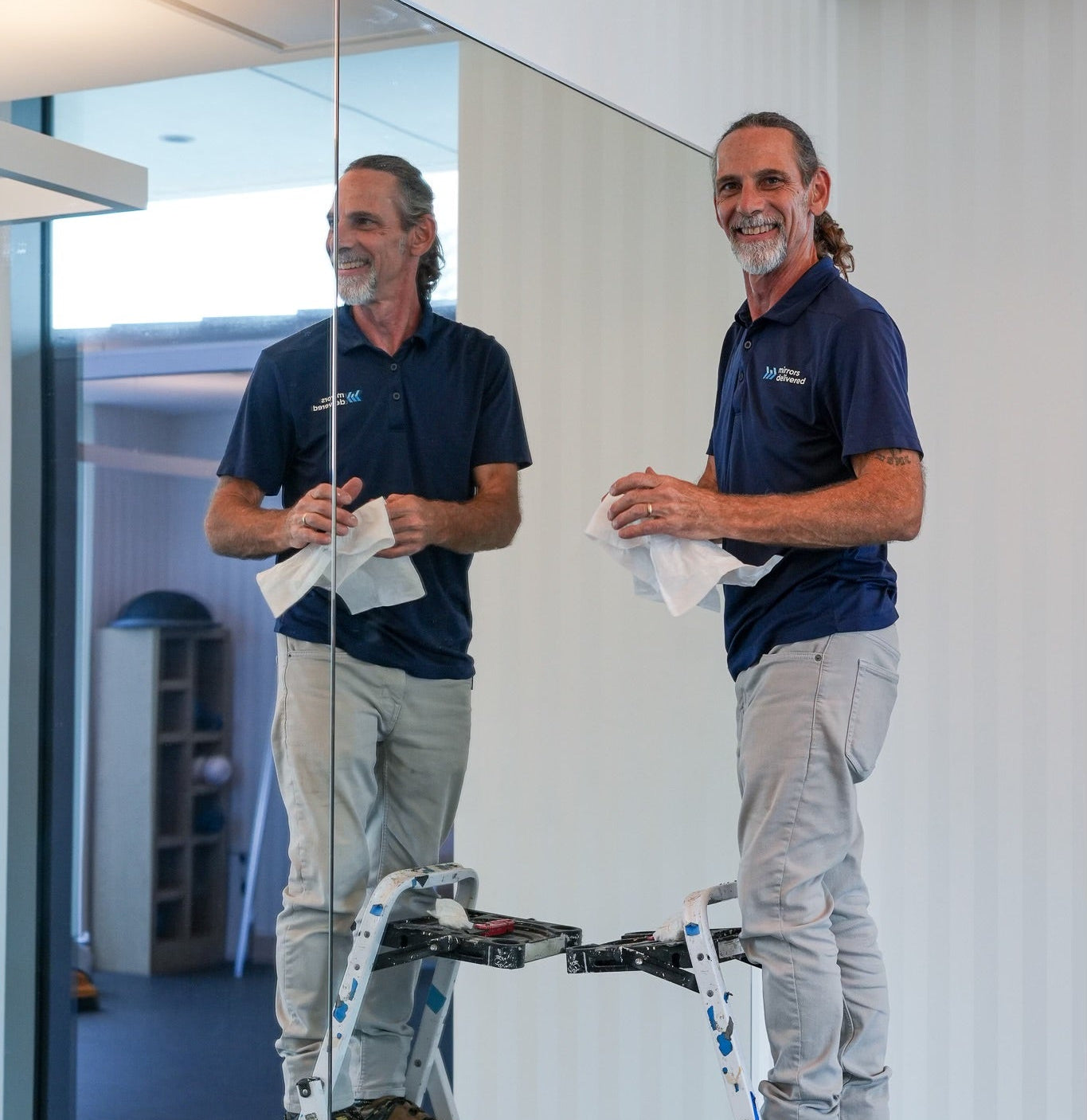 Mirror Installer on ladder cleaning a large mirror in a modern fitness center