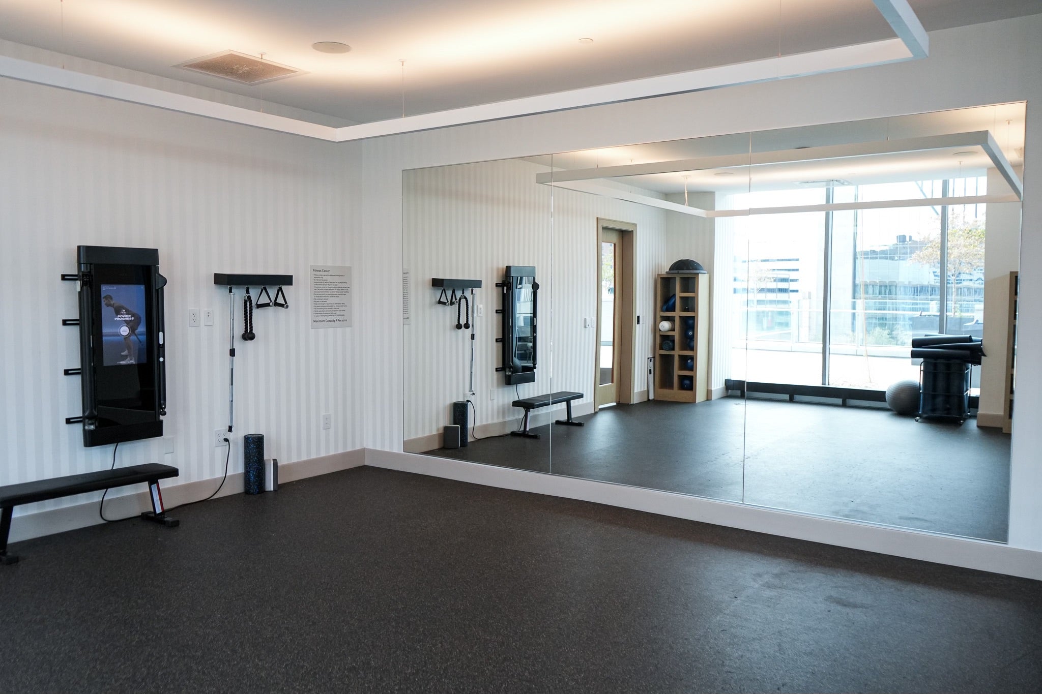 Gym room with exercise equipment, mirrors, and large windows.