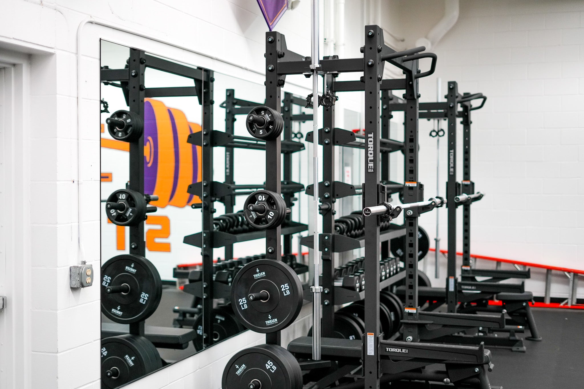 Gym equipment including mirrors weight racks and dumbbells in a fitness center.